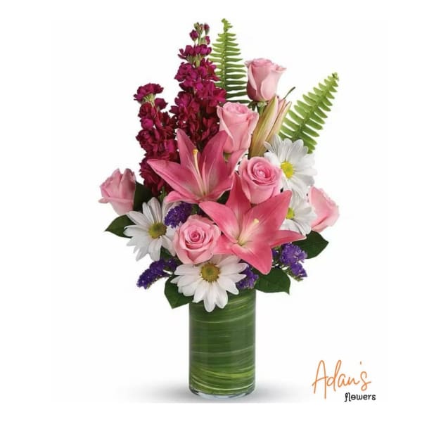 Pink roses and lilies arranged with white daisies in a green glass vase