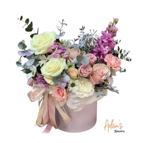 Pastel bouquet of roses, carnations, and purple blooms in a pink hatbox