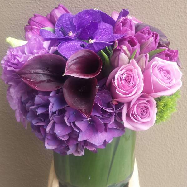 Purple bouquet with roses, hydrangea, calla lilies, and orchids in a glass vase