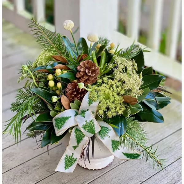 Holiday arrangement in a white vase with pinecones and a ribbon