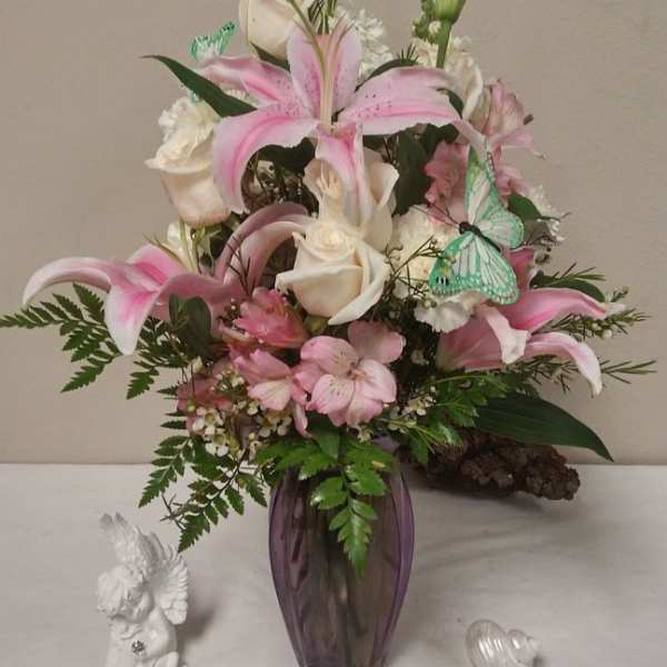 Pink lilies and white roses arranged in a purple vase with butterfly picks
