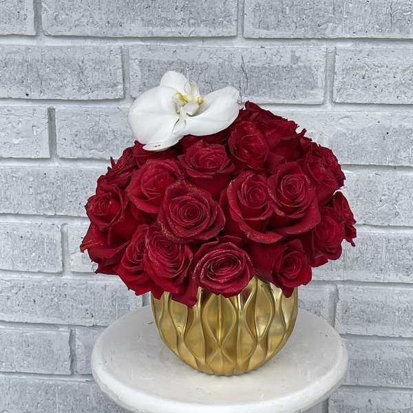 Red roses in a gold vase with a white orchid accent
