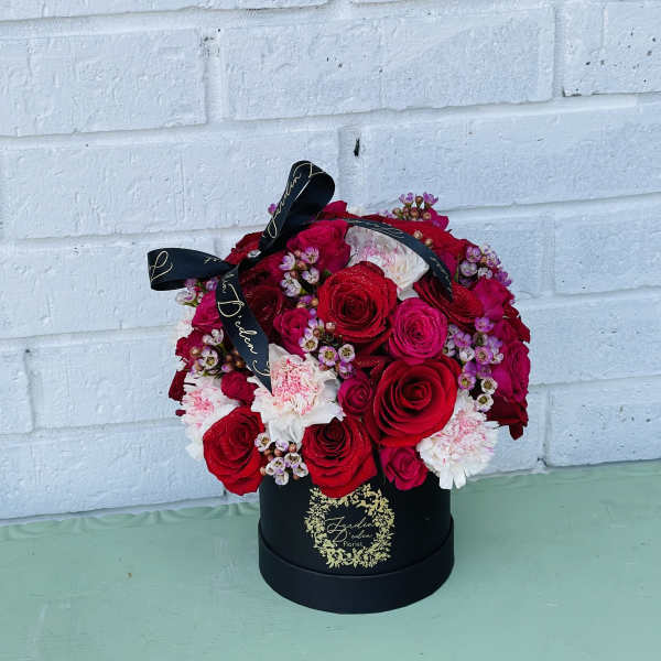 Red and pink rose arrangement in a black hat box with ribbon