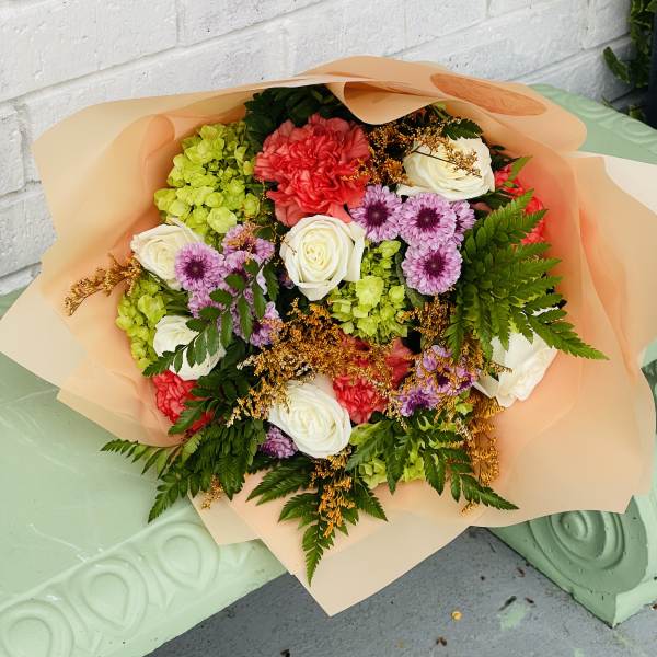 Mixed bouquet of roses, carnations, and purple daisies wrapped in peach paper