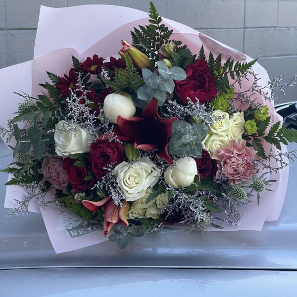 Mixed bouquet of roses, lilies, and carnations wrapped in pink paper