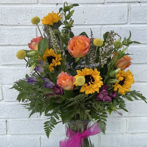 Bouquet of sunflowers, orange roses, and purple flowers in a glass vase