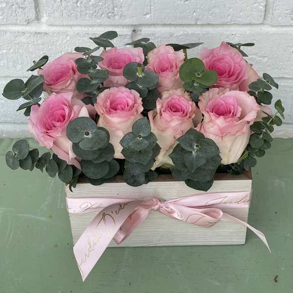 Pink roses arranged in a rectangular box with eucalyptus and a pink ribbon