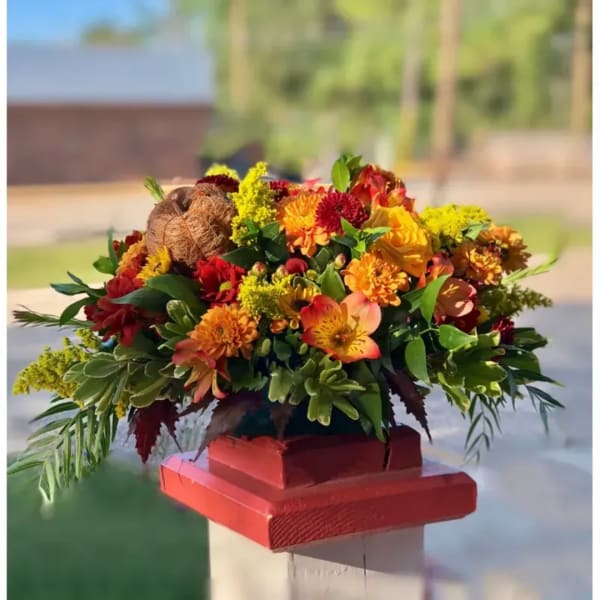 Autumn floral arrangement with orange and red blooms in a red container
