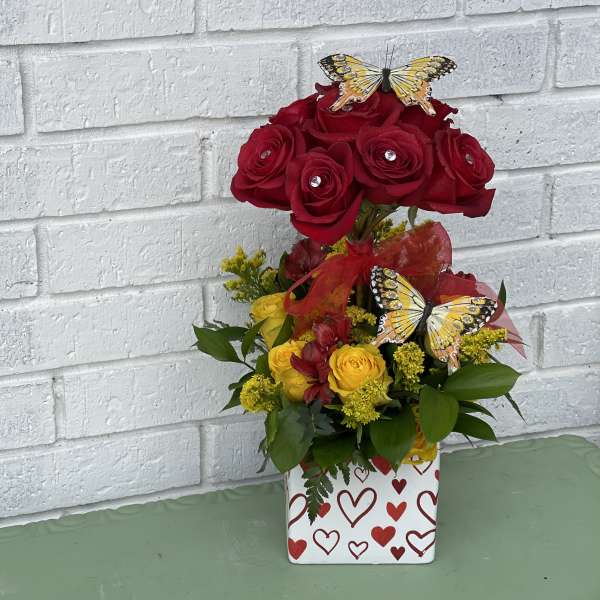 Red and yellow rose arrangement in a heart-patterned box with butterfly picks