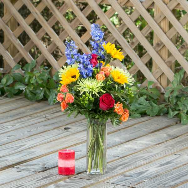Colorful mixed flower arrangement in a tall glass vase with a red candle nearby