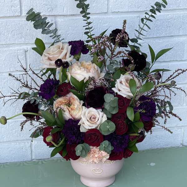 Bouquet of roses and dark blooms in a pale vase