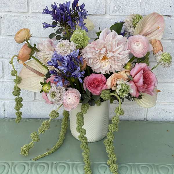 Mixed pastel bouquet in a white vase with trailing green stems