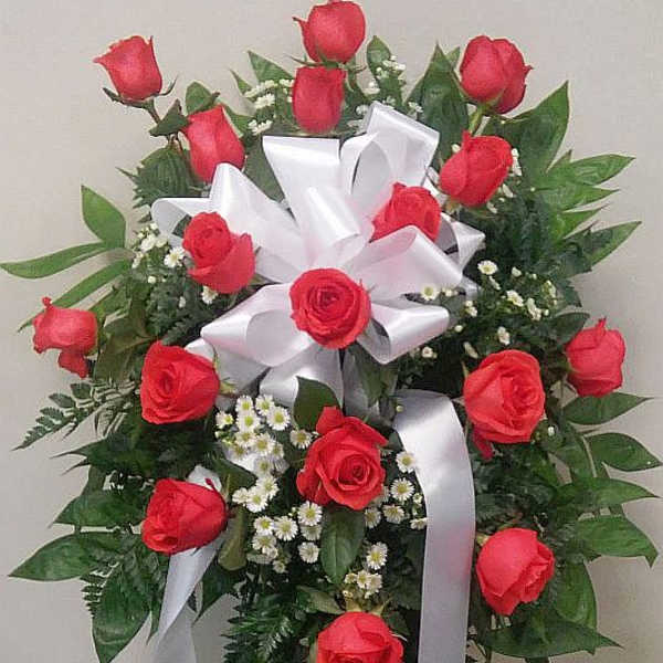 Standing spray of red roses with white ribbon and small white filler flowers
