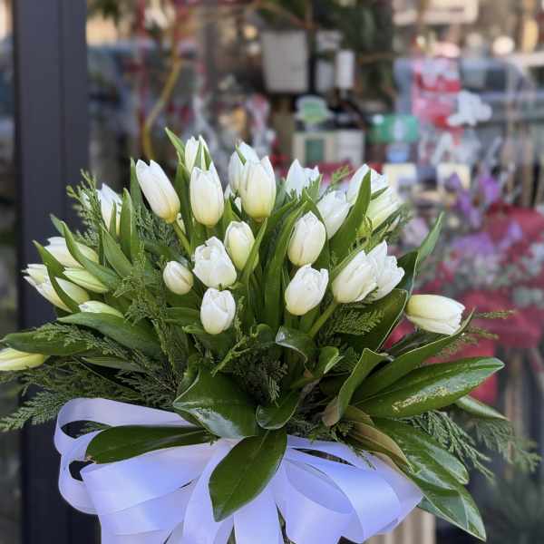 White tulip bouquet in a clear glass vase with a lavender ribbon