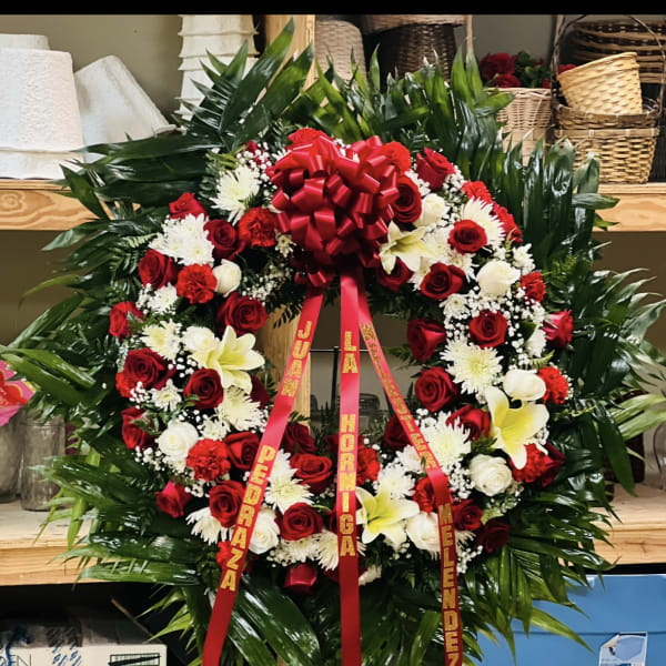 Large red and white funeral wreath on a stand with ribbon streamers