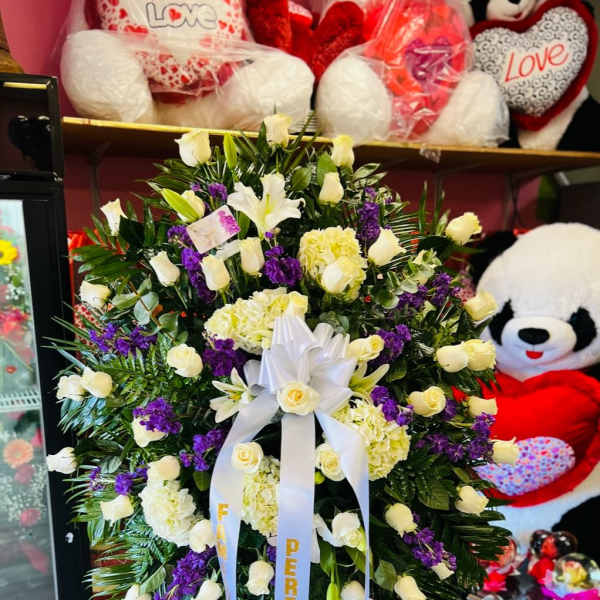 Large standing floral spray with white roses, lilies, and purple flowers on a ribboned easel