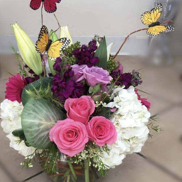 Pink roses and white hydrangeas with butterfly picks in a glass vase