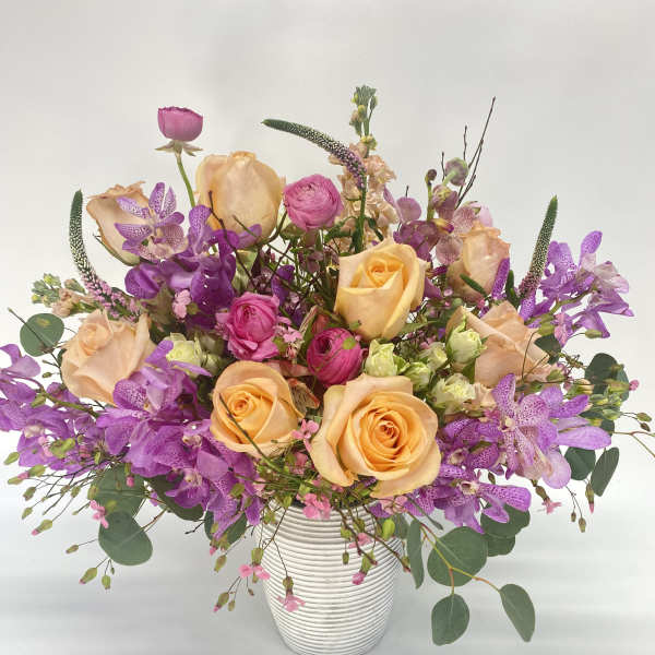 Mixed bouquet of peach roses and purple orchids in a white vase