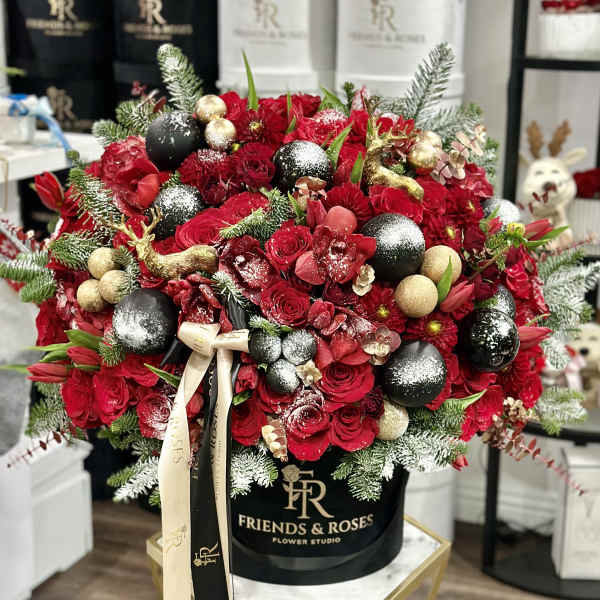 Red rose arrangement in a black hat box with gold ornaments and ribbon