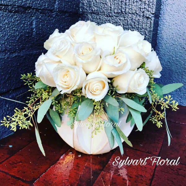 White rose bouquet in a white vase with trailing greenery