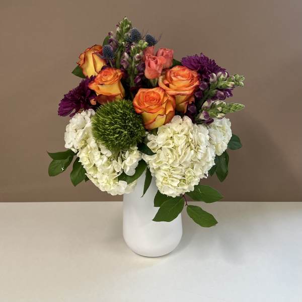 Bouquet of orange roses, white hydrangeas, and purple flowers in a white vase