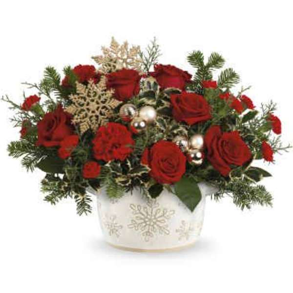 Red roses arranged in a white snowflake vase with holiday accents