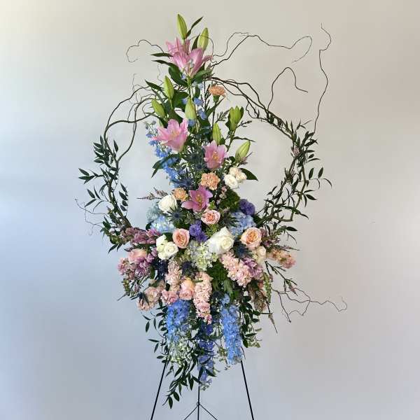 Tall floral spray with pink lilies, roses, and blue flowers on a stand