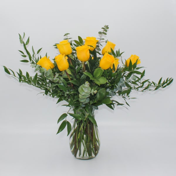 Yellow roses in a clear glass vase with greenery