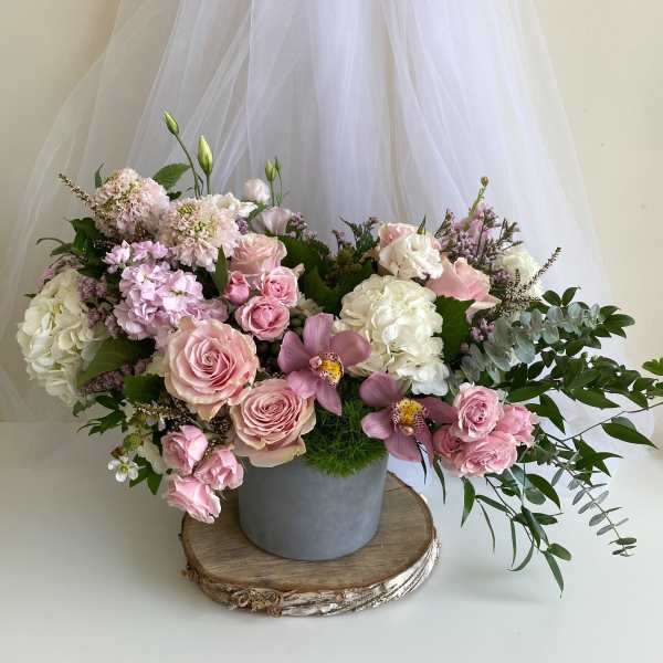 Pink and white floral arrangement in a gray vase with trailing greenery