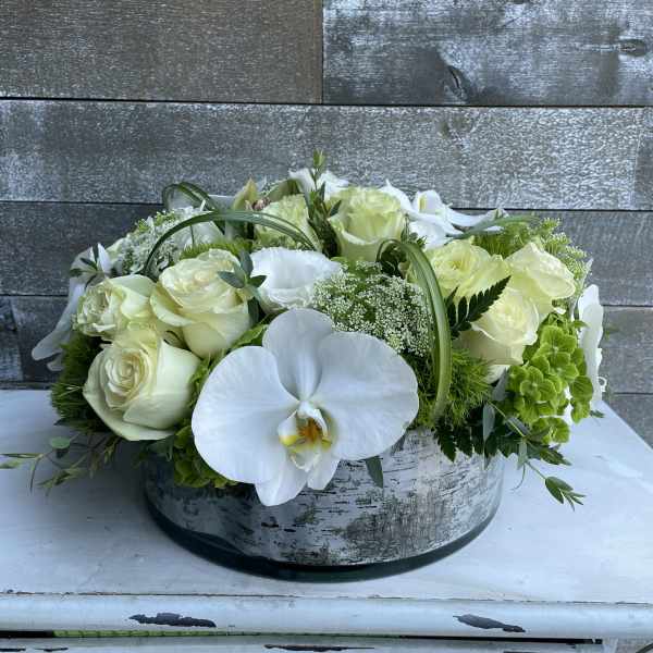 White roses and orchids arranged in a low round box
