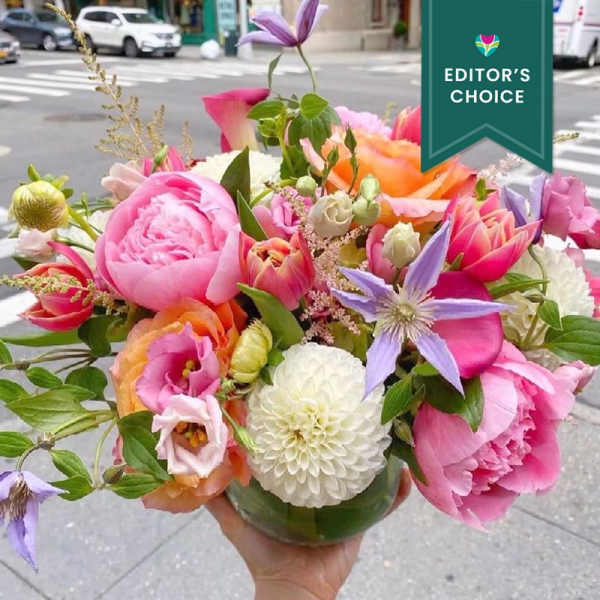 Handheld bouquet of pink, orange, and purple flowers in a glass vase