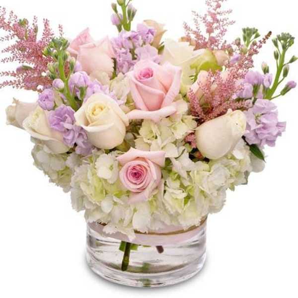 Pastel bouquet of roses, hydrangeas, and lavender flowers in a clear glass vase