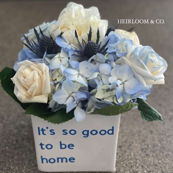 Blue and white floral arrangement in a white vase with text