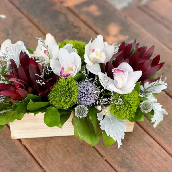 White orchids and burgundy flowers arranged in a wooden box