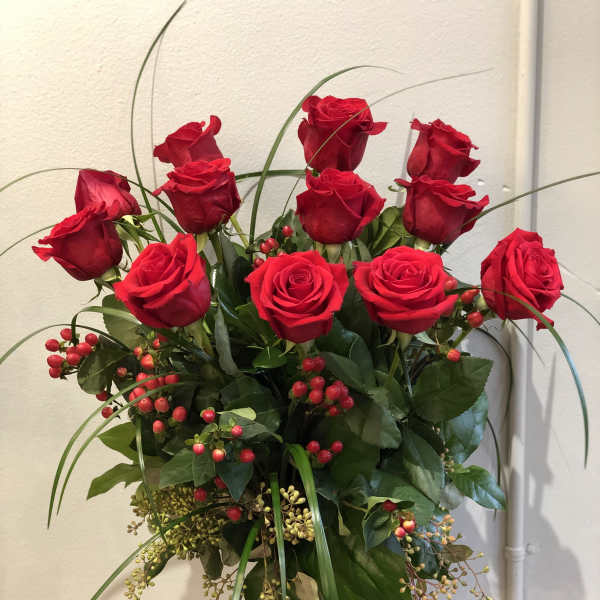 Red roses arranged in a clear glass vase with berries and greenery