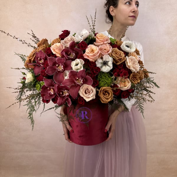 Large hatbox arrangement of red orchids, mixed roses, and white anemones in a burgundy container.