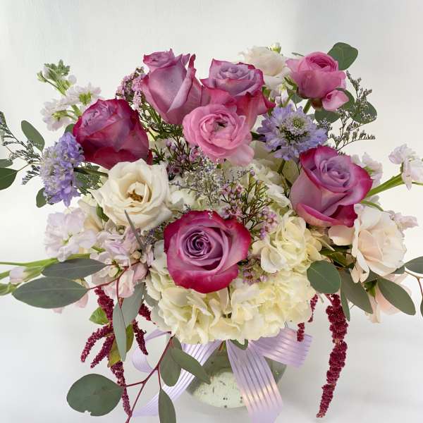 Bouquet of pink and white roses in a glass vase with a lavender ribbon