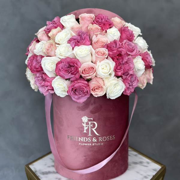 Pink and white roses arranged in a round velvet hat box