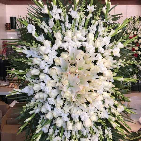 Large white funeral spray with lilies, roses, and orchids