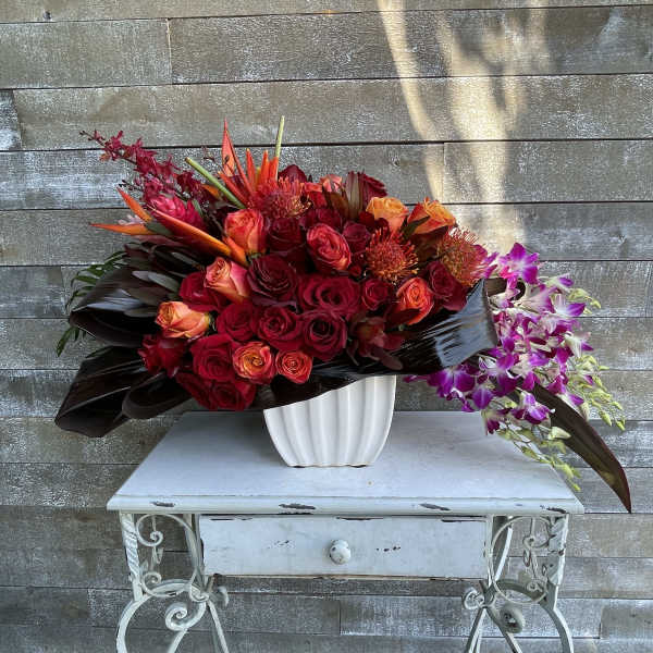Large red and orange floral arrangement in a white vase with purple orchids