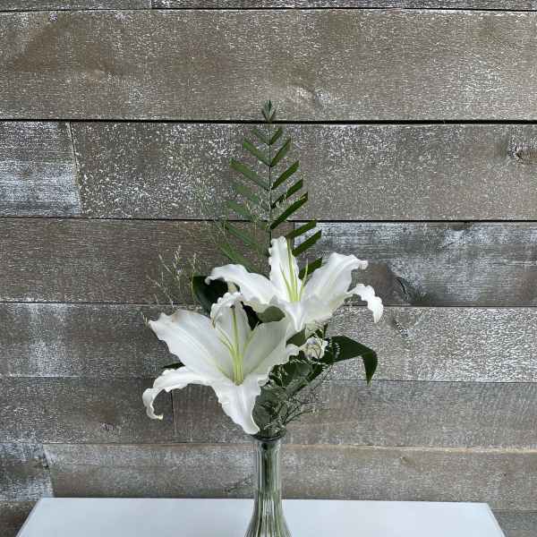 White lilies in a clear glass vase with greenery
