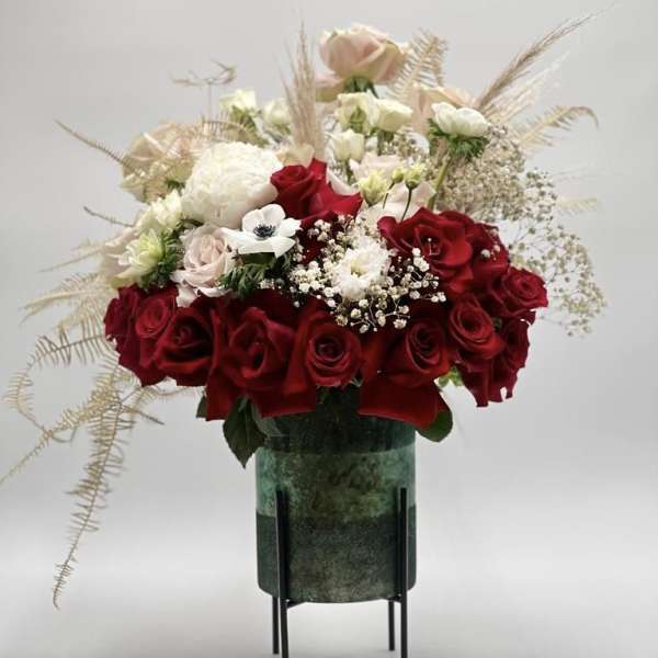 Red and white rose arrangement in a green vase on a stand