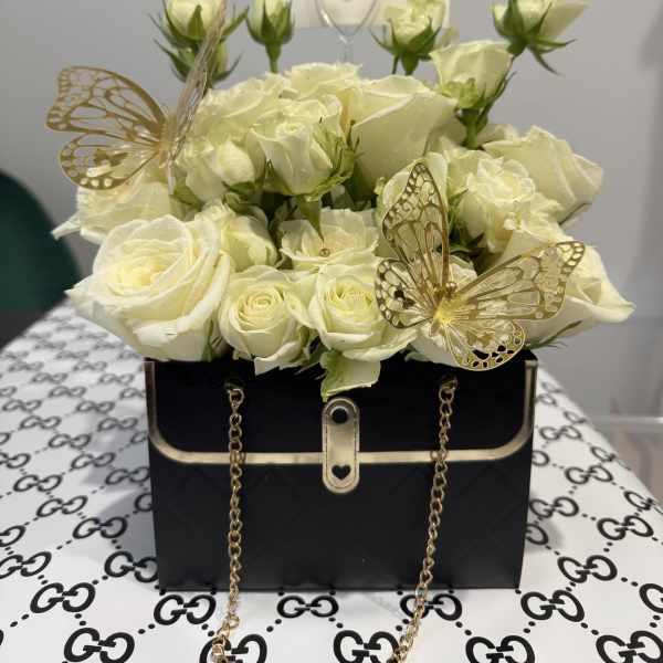 Cream roses arranged in a black handbag-style box with gold butterfly accents