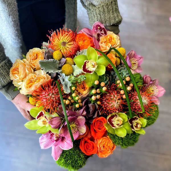 Handheld bouquet of orange roses and green orchids with pink blooms