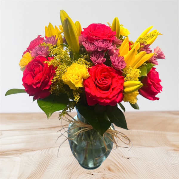 Bouquet of red roses, yellow lilies, and purple daisies in a glass vase