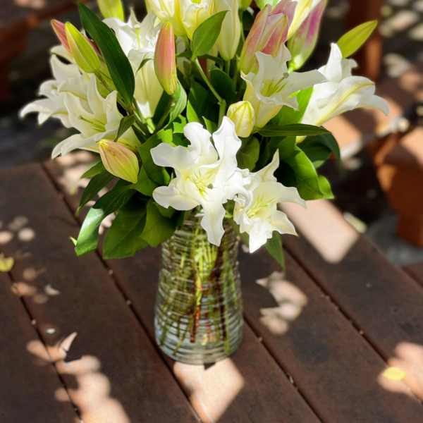 White lilies in a clear glass vase on a wooden table