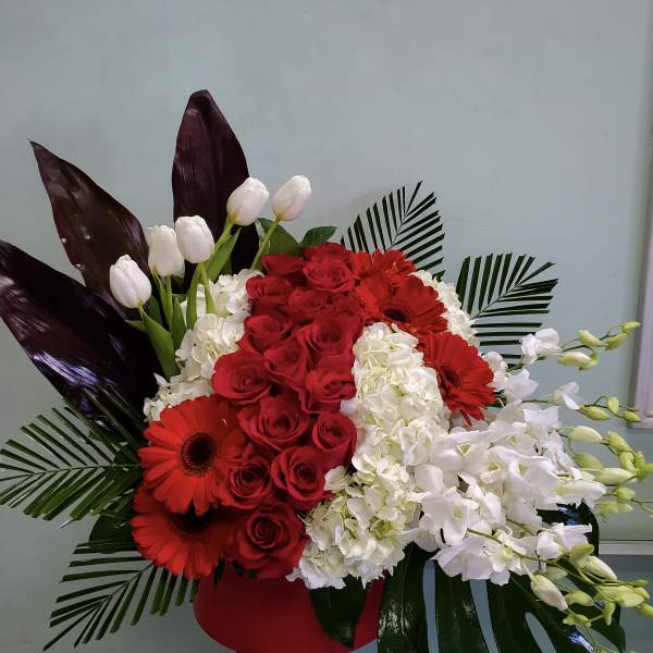 Red roses and gerbera daisies with white orchids in a red vase