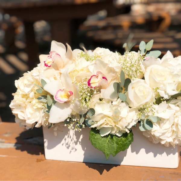 White floral arrangement in a rectangular vase with orchids and roses