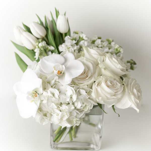 White roses, orchids, and tulips arranged in a clear square vase