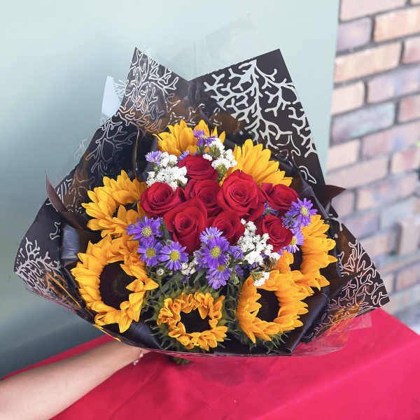 Bouquet of red roses, sunflowers, and purple daisies wrapped in black paper
